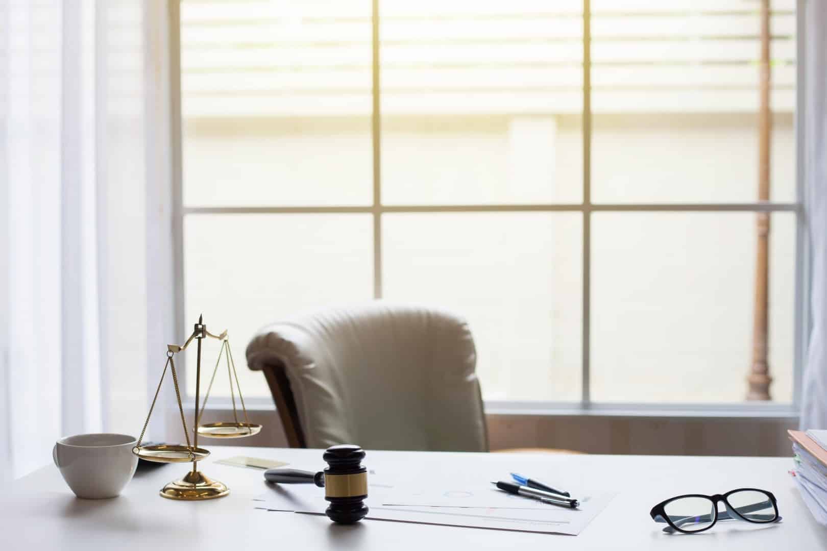 Scales of justice and a gavel on a desk by a window